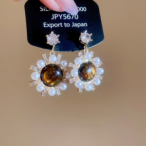 Close-up of vintage tiger eye stud earring with pearls and zircons on black card