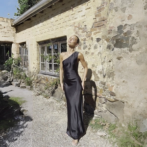Detail of elegant black satin one-shoulder dress with high slit and silky finish