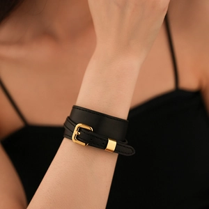 Close-up of a stylish black faux leather wrap bracelet with a polished gold buckle