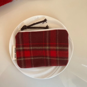 Detail of red and black tartan wool coin purse with a braided zipper pull and logo tag