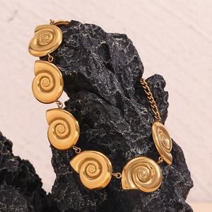 Artistic close-up of a gold-plated snail shell chain necklace on a dark natural rock