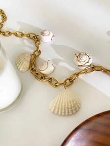 Macro detail of gold chunky chain necklace with natural shell and conch pendants