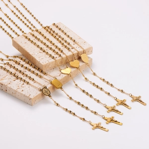 Golden stainless steel rosary necklaces with crucifix pendants on stone display