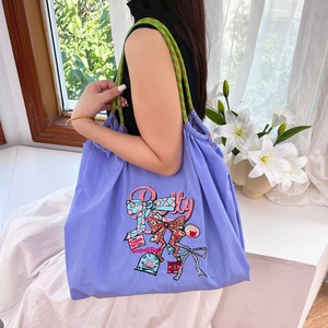 Detail of purple nylon tote bag with colorful embroidery and woven strap in bright setting