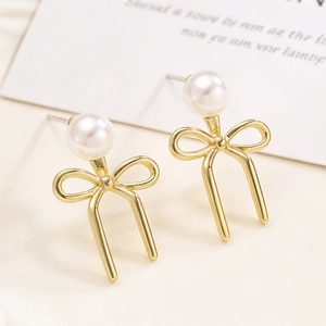 Close-up of golden bow-shaped stud earring with a round pearl on a minimalist background