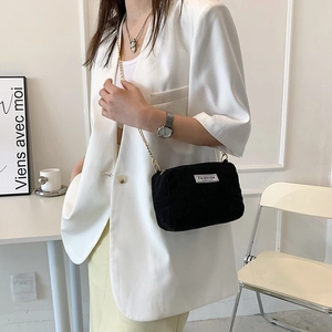 Detail of black corduroy crossbody bag with golden chain strap on white blazer