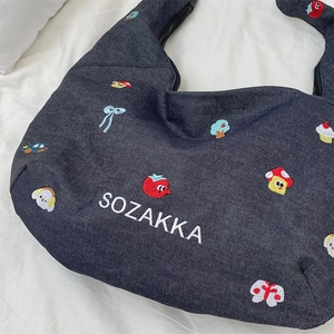 Detail of blue denim hobo bag featuring colorful embroidered mushroom and cupcake motifs