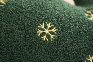 Macro shot of dark green fleece fabric with delicate gold embroidered snowflake patterns