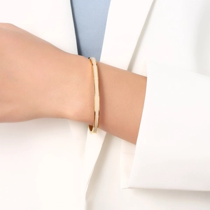 Minimalist gold bangle with cream enamel inlay shown on wrist with a professional outfit