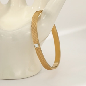 Minimalist gold plated stainless steel bangle with white square inlay on model
