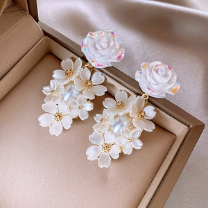 Detailed macro view of white 3D flower earrings with faux pearls on champagne silk