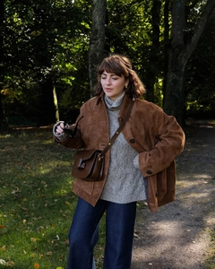Gros plan détaillé d'une veste en daim marron portée avec un pull à col roulé gris
