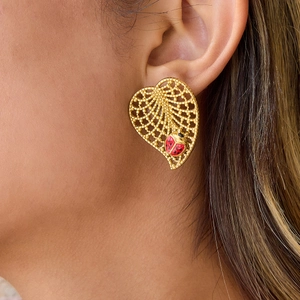Golden heart cutout earrings with enamel ladybug pendant worn by a model