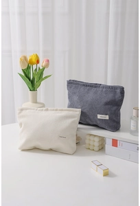 Detail of minimalist corduroy makeup bags in beige and dark grey on a desk