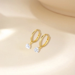 Macro shot of gold hoop earrings featuring square-cut clear crystals on soft fabric