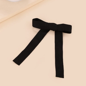 Elegant black fabric bow hair clip with ribbons on a minimalist beige background