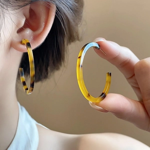 Close-up of amber resin C-shaped hoop earrings with tortoiseshell pattern on model