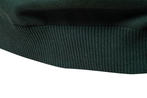 Close-up of dark green ribbed knit texture on the hem and cuff of the sweater
