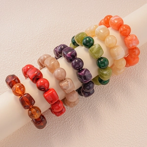 Detail of colorful marble-textured acrylic bead bracelets on a white cylinder stand