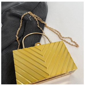Close-up of golden rectangular evening clutch with geometric V-stripes and pearl clasp