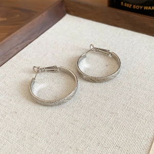 Detailed view of silver hoop earrings with a matte textured twill pattern on a tray