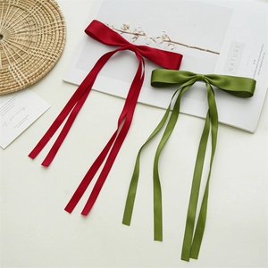 Detail of red and green satin bow hair clips with long ribbons on a minimalist background