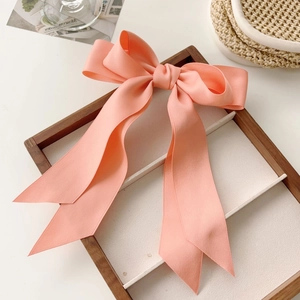 Detailed close-up of a pink large bow hair clip with ribbons on a wooden tray