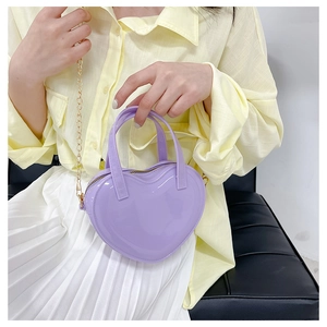 Detail of a purple heart-shaped jelly handbag with gold chain strap held by a model