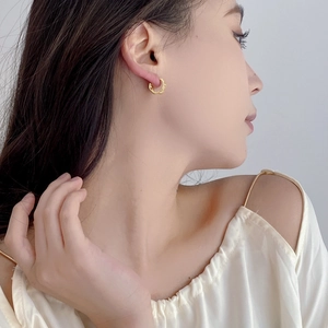 Close-up of a minimalist gold geometric diamond-shaped hoop earring worn by a model