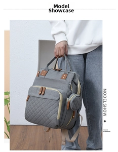 Gray quilted diaper backpack with brown leather details and round side pouch for mothers