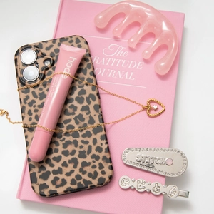 Flat lay of a gold heart pendant necklace with leopard case and beauty accessories