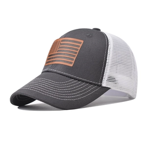 Dettaglio di un cappello trucker grigio con patch in pelle bandiera USA e rete bianca