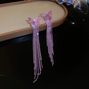 Detail of long butterfly tassel earrings with purple beads on a beige jewelry display