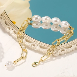 Close-up of baroque pearl bracelet with gold paperclip chain on a marble surface