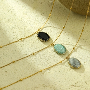 Elegant gold necklaces with oval natural stones in black and green on stone background