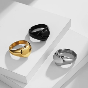 Three heart-shaped minimalist rings in gold, silver, and black on white stone blocks