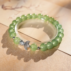 Close-up of light green jade beads and silver fish charm on a round jewelry stand