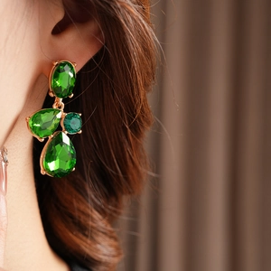 Close-up of vintage gold geometric drop earrings with green crystals on a model