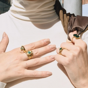 Détail de mains féminines portant diverses bagues en or avec des malachites vertes