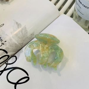 Elegant acetate hair claw clip with green and yellow marble patterns on white magazine background