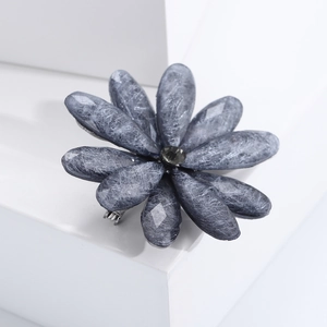 Macro detail of a grey acrylic flower brooch with a central dark gemstone on a white base