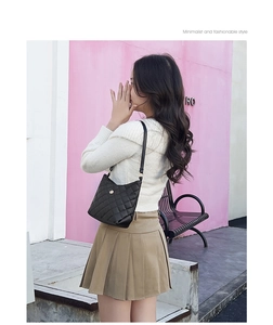 Detail of black quilted shoulder bag featuring metal flower buckle on model in outdoor setting