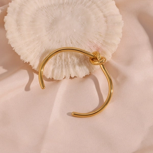 Detailed macro view of gold-plated knot bracelet on soft pink silk and white coral