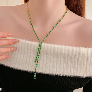 Detail of elegant gold Y-shaped necklace with green gemstone tassel on a model