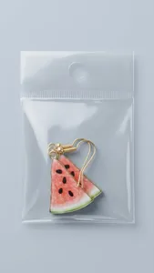 Close-up of translucent watermelon drop earrings with gold hooks in clear packaging