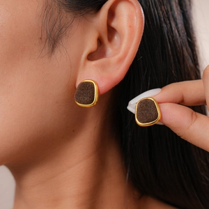 Detail of vintage gold-rimmed flocked square stud earrings worn on a model's ear