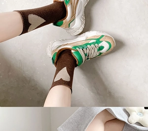 Detail of dark brown mid-calf socks with cream heart patterns and chunky sneakers