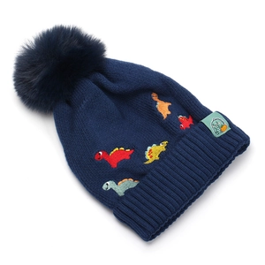 Détail du bonnet en tricot bleu marine avec broderie dinosaure et pompon en fausse fourrure