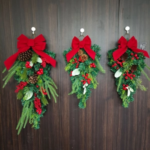 Close-up of three teardrop Christmas wreaths with red bows and pinecones on a door