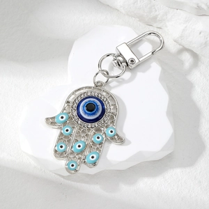 Detail of silver Hamsa hand keychain with blue evil eye beads on white stone